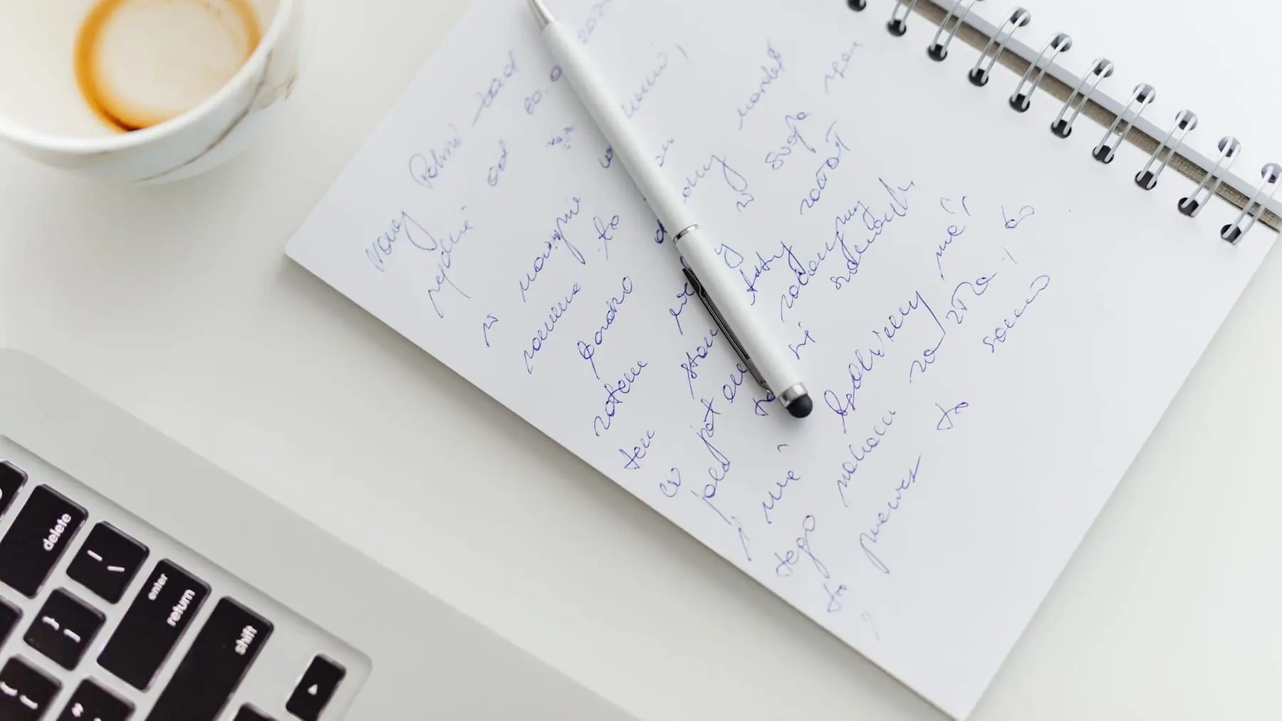 A notebook with handwritten plans next to a laptop and a coffee