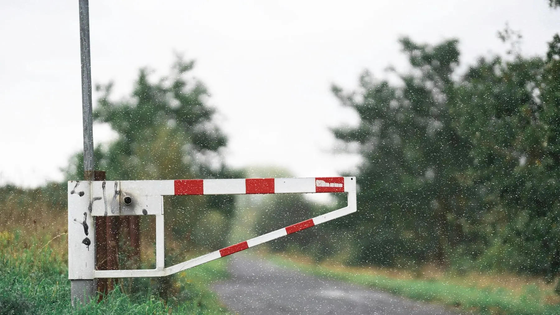 A red and white road barrier arm across a country road